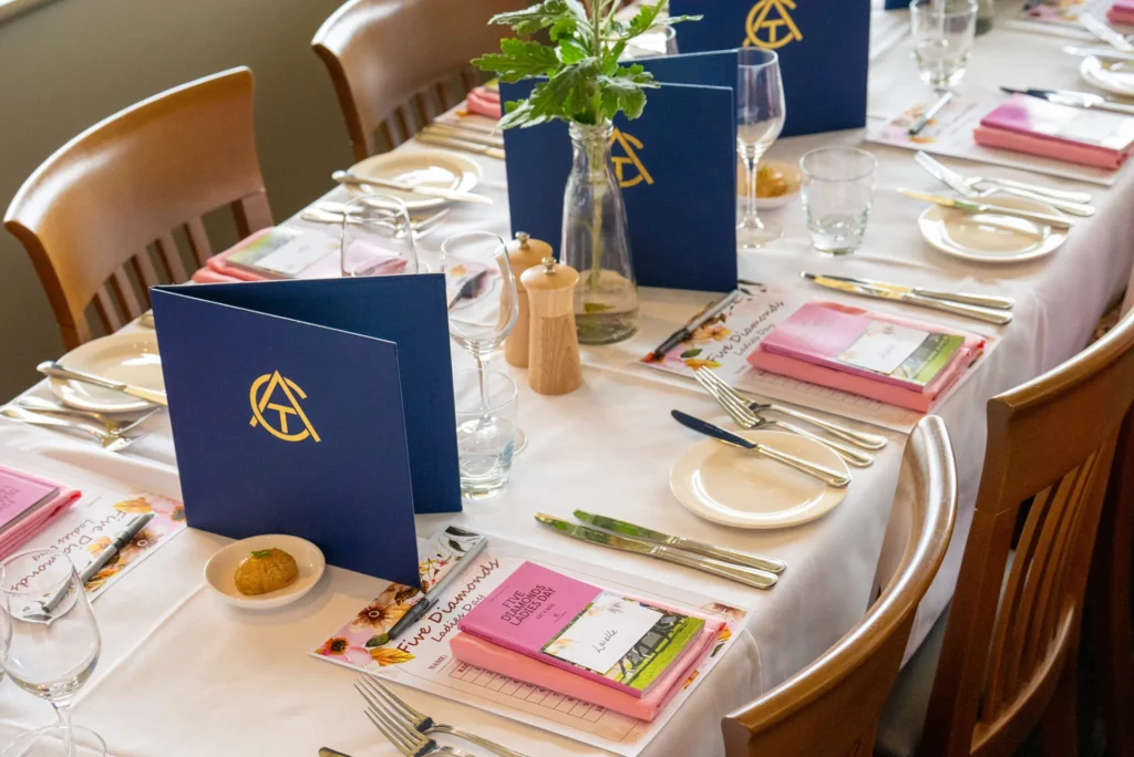 A table set for a ladies’ day lunch with navy menus and pink racebooks.